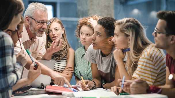 Mature teacher teaching group of college students at campus.